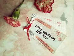 Papierowa rocznica. Kupony miłości dla Ciebie, przewiązane czerwoną nitką, obok dwóch goździków.