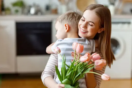 Uśmiechnięta mama tuli synka z bukietem różowych tulipanów. To z pewnością wyjątkowe życzenia urodzinowe dla mamy.