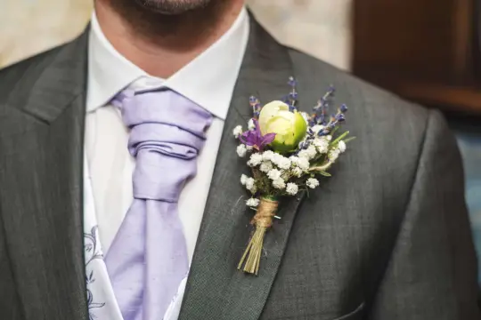 Elegancka szara marynarka z lawendowym krawatem i delikatną butonierką z białych kwiatów i lawendy.
